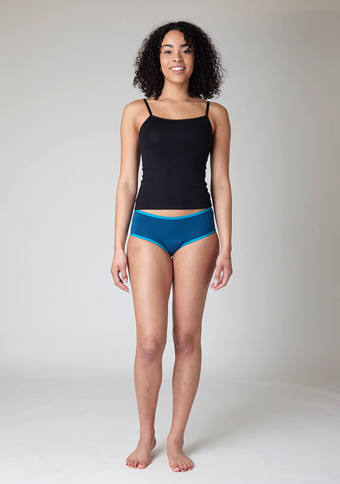 Front image of a five foot ten, size 10 model wearing Ugly Pants' Teal Hipster Brief Period Pants in light to moderate  absorbency, paired with a black cami top