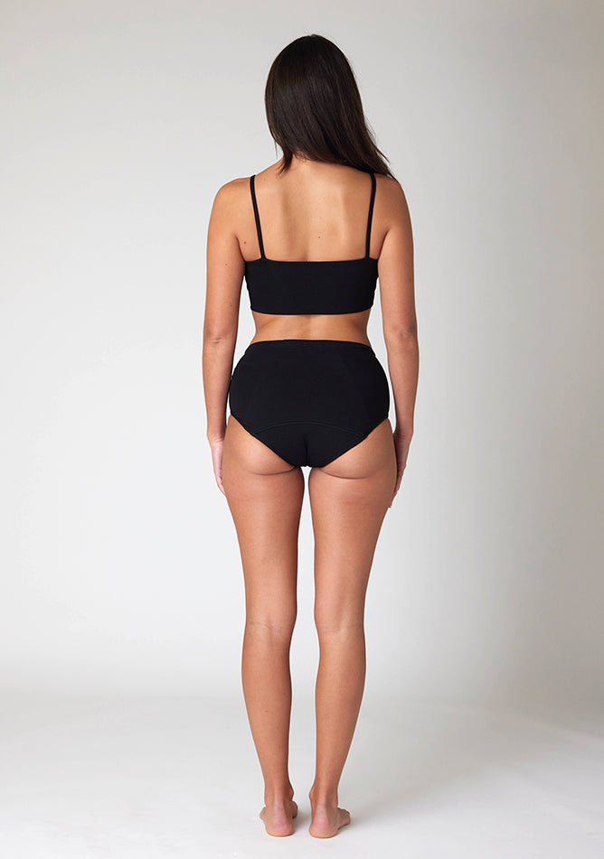 Back image of a five foot ten, size 10=0 model wearing Ugly Pants' Black Overnight flow sleep set with matching black crop top, featuring a self tie detachable bow, but a straight neckline