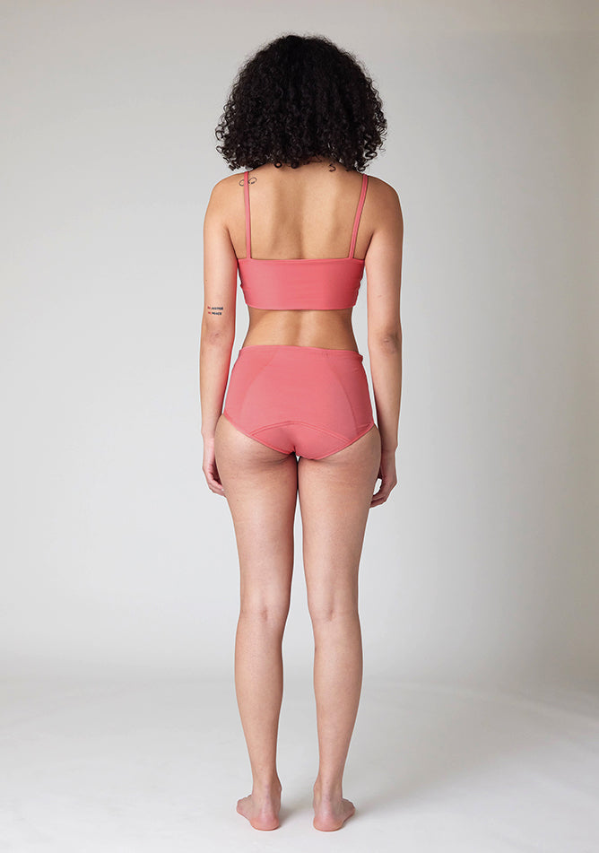 Back image of a five foot ten size 10 model wearing Ugly Pants' Coral Overnight flow sleep set with matching coral crop top, this image does not feature the self tie bow, but a straight neckline. 