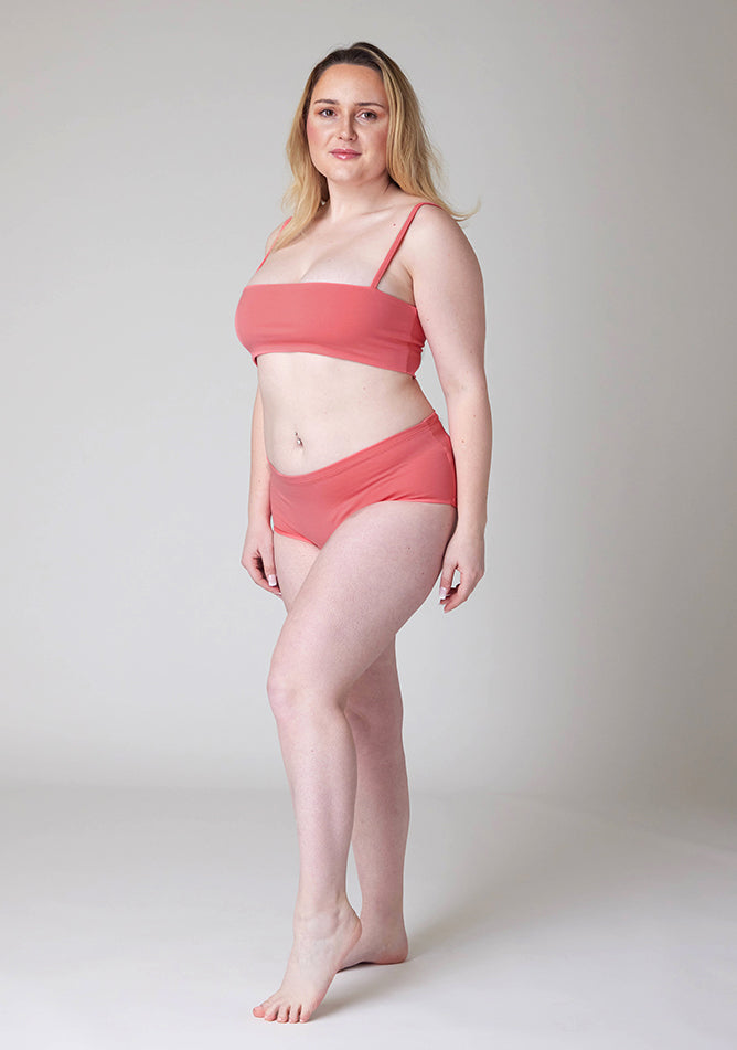 Quarter front image of a five foot three size 12 model wearing Ugly Pants' Coral Overnight flow sleep set with matching coral crop top, this image does not feature the self tie bow, but a straight neckline. 