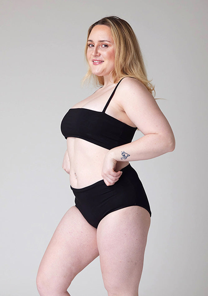 Close up quarter front image of a model wearing Ugly Pants' Black Overnight flow sleep set with matching black crop top, this image does not feature the self tie bow, but a straight neckline.