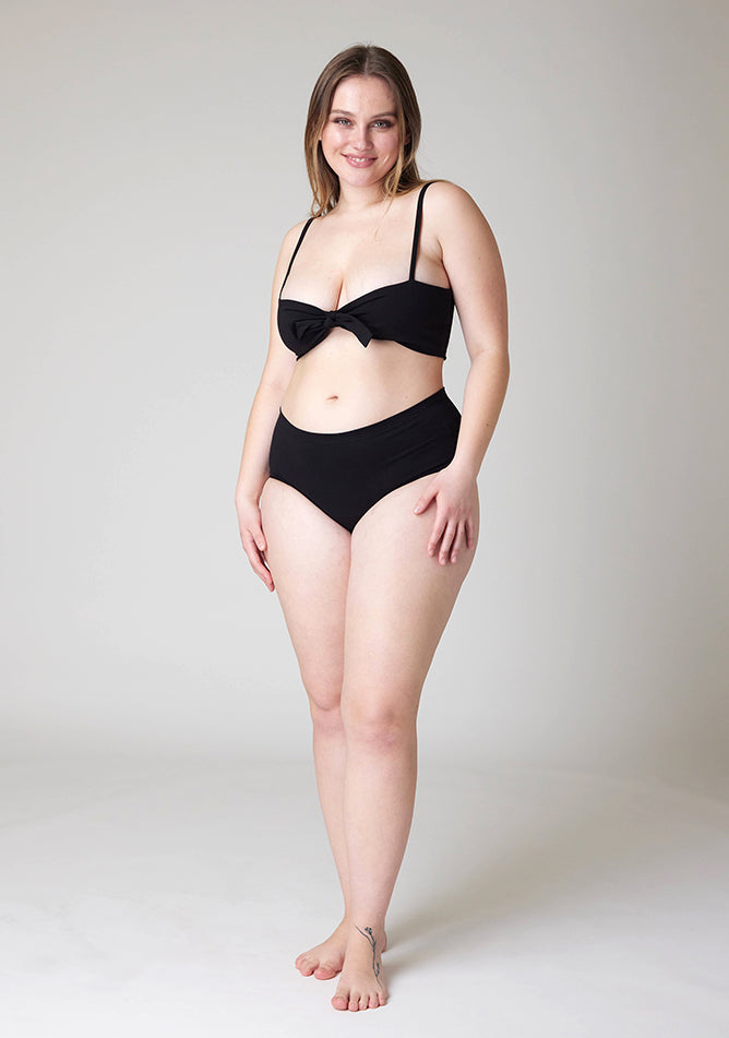 Front image of a five foot five, size 14 model wearing Ugly Pants' Black Overnight flow sleep set with matching black crop top, featuring a self tie detachable bow.