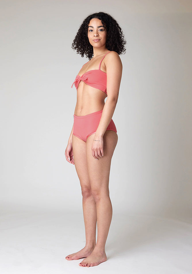 Quarter front image of a five foot ten, size 10 model wearing Ugly Pants' Coral Overnight flow sleep set with matching coral crop top, featuring a self tie detachable bow.