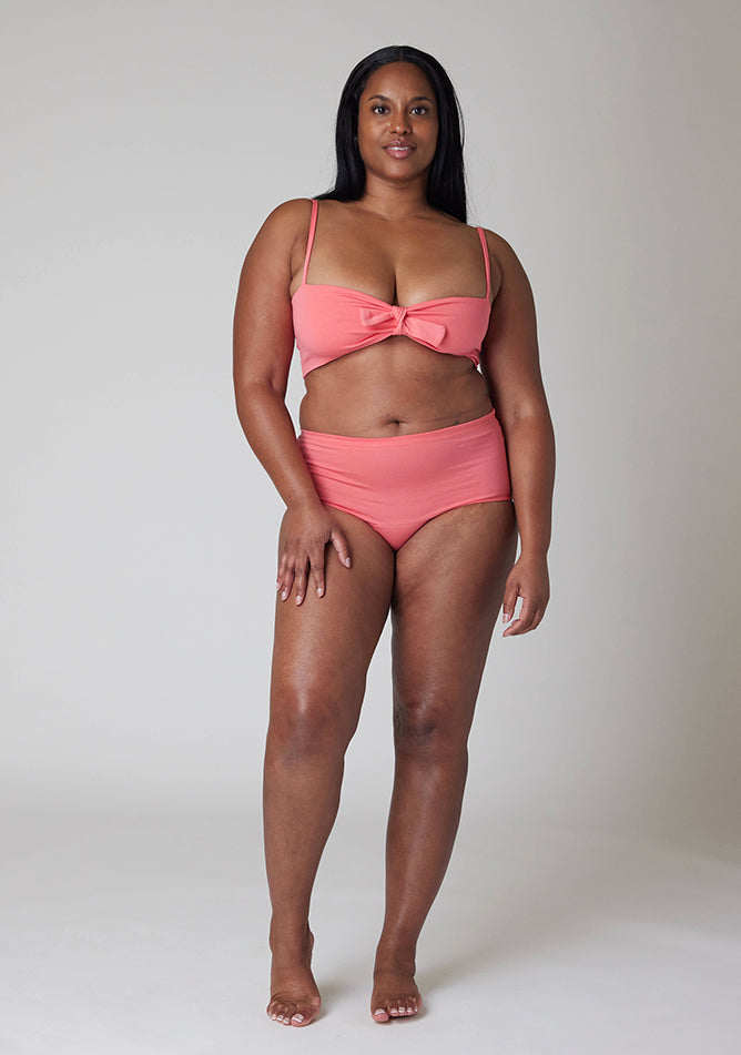 Front image of a five foot five, size 10 model wearing Ugly Pants' Coral Overnight flow sleep set with matching coral crop top, featuring a self tie detachable bow.