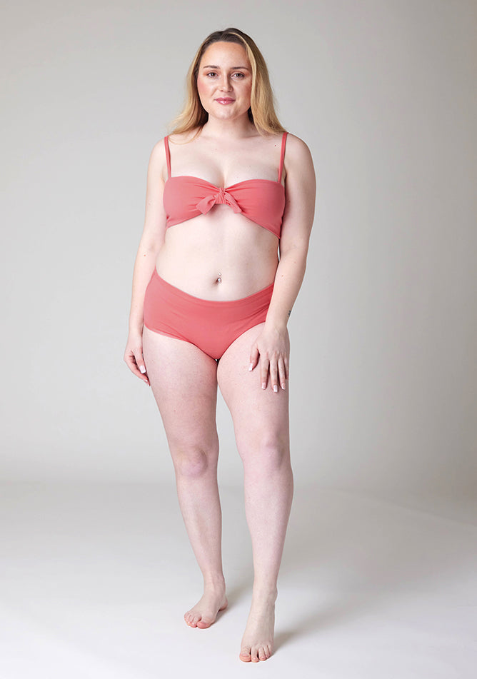 Front image of a five foot three, size 12 model wearing Ugly Pants' Coral Overnight flow sleep set with matching coral crop top, featuring a self tie detachable bow.