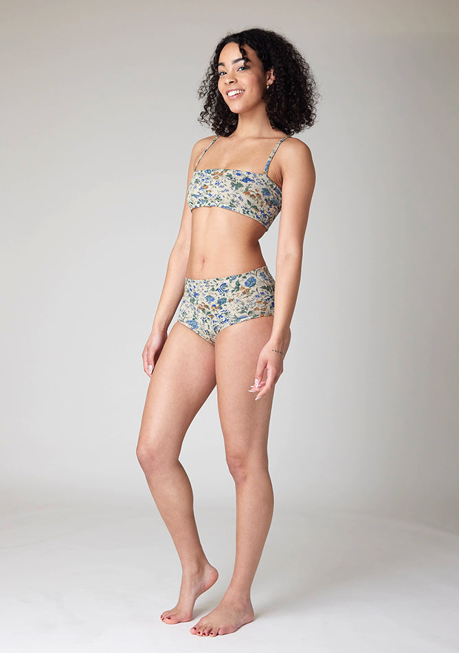 Quarter front image of a model wearing Ugly Pants' Cream Floral Print Overnight period pants in moderate to heavy absorbency, paired with a cream floral print crop top, with a self tie detachable bow, this image does not feature the self tie bow, but a straight neckline.