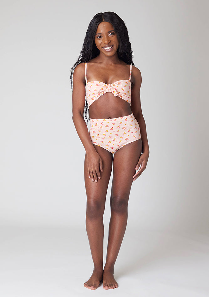 Front image of a five foot, size 6 model wearing Ugly Pants' Pink Floral Print Overnight period pants in moderate to heavy absorbency, paired with a pink floral print crop top, with a self tie detachable bow.