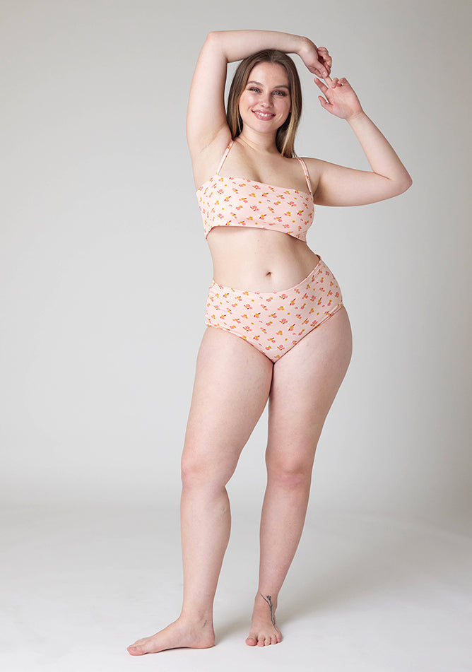 Front image of a five foot five, size 14 model wearing Ugly Pants' Pink Floral Print Overnight period pants in moderate to heavy absorbency, paired with a pink floral print crop top, with a self tie detachable bow, this image does not feature the self tie bow, but a straight neckline.