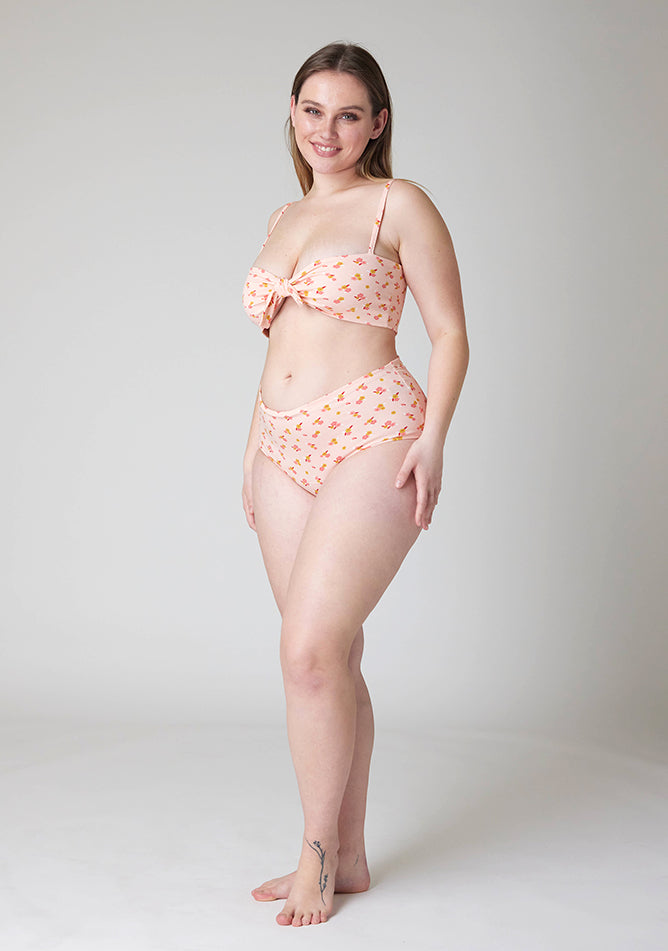 Quarter front image of a five foot five, size 14 model wearing Ugly Pants' Pink Floral Print Overnight period pants in moderate to heavy absorbency, paired with a pink floral print crop top, with a self tie detachable bow.