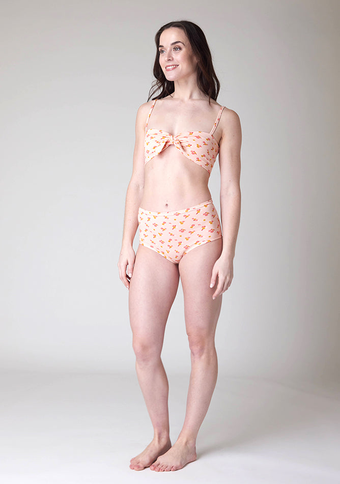 Quarter front image of a five foot nine, size 8 model wearing Ugly Pants' Pink Floral Print Overnight period pants in moderate to heavy absorbency, paired with a pink floral print crop top, with a self tie detachable bow.