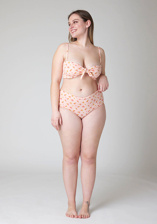 Front image of a five foot five, size 14 model wearing Ugly Pants' Pink Floral Print Overnight period pants in moderate to heavy absorbency, paired with a pink floral print crop top, with a self tie detachable bow.