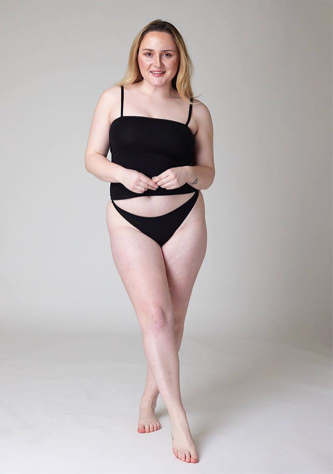 Front image of a five foot three, size 12 model wearing Ugly Pants' Black Thong period pants in a light absorbency, paired with a black cami top.