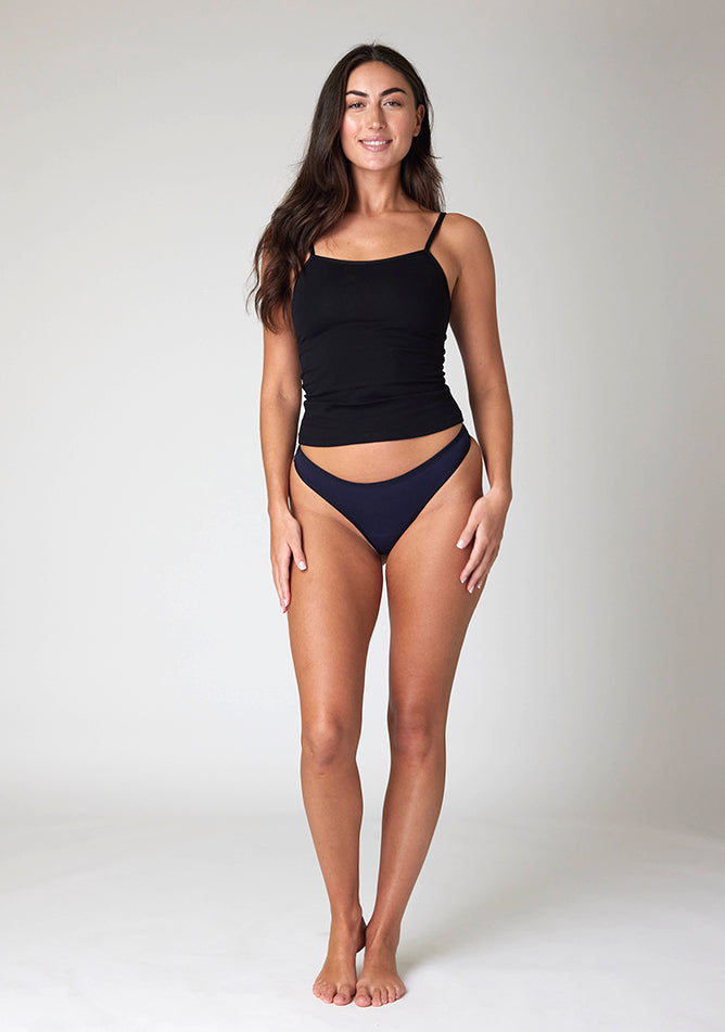 Front image of a five foot ten, size 10 model wearing Ugly Pants' Navy Thong period pants in a light absorbency, paired with a black cami top.
