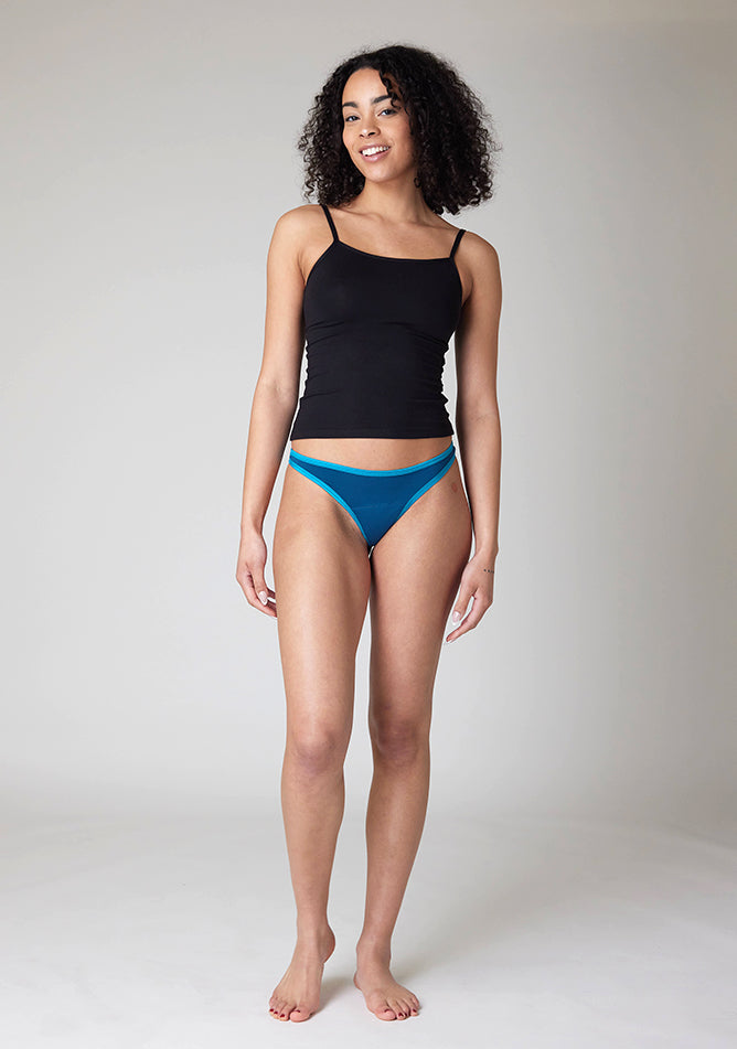 Front image of a five foot ten, size 10 model wearing Ugly Pants' Teal Thong period pants in a light absorbency, paired with a black cami top.