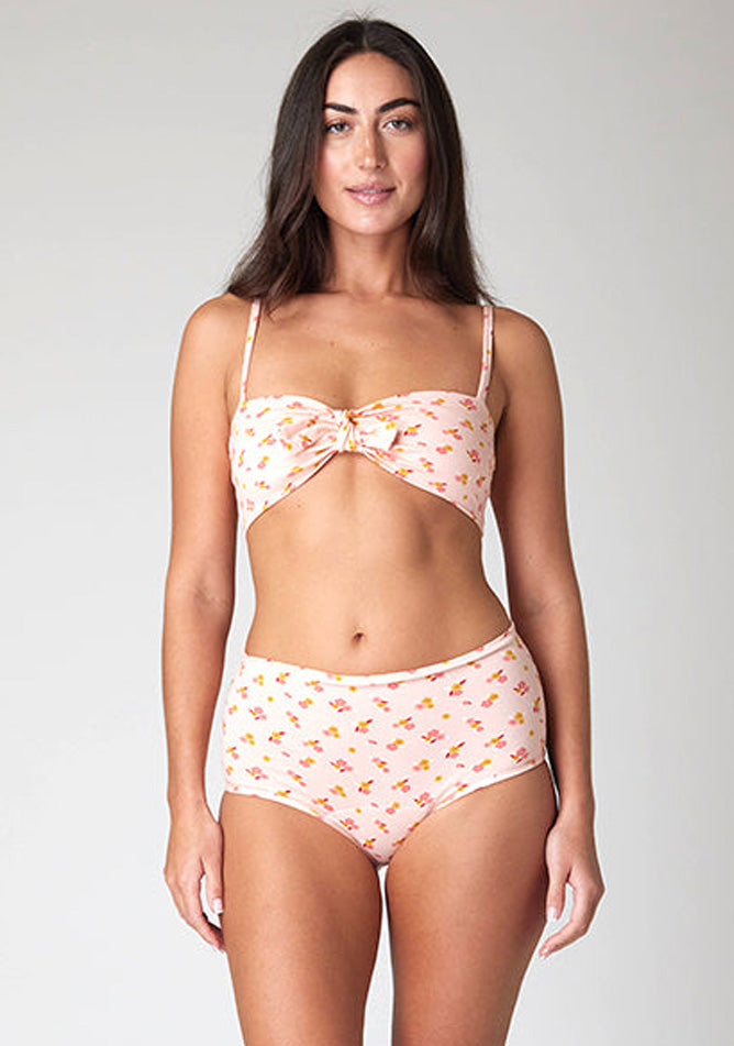 Close-up image of a five-foot-ten, size 10 model wearing Ugly Pants' Pink Floral Print Overnight period pants in moderate to heavy absorbency, paired with a pink floral print crop top, with a self tie detachable bow.