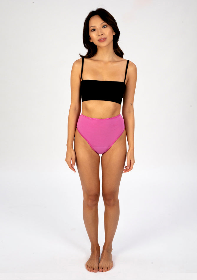 Front image of a five foot three, size 6 model wearing Ugly Pants' pink high waisted period pants in light to moderate absorbency, paired with a black crop top.
