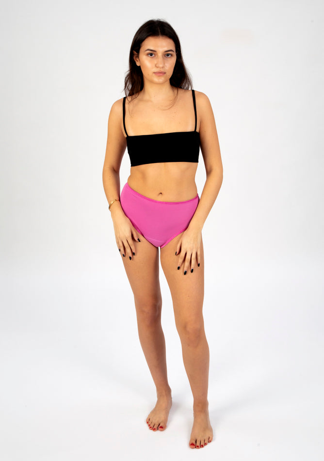 Front image of a five foot six, size 8 model wearing Ugly Pants' pink high waisted period pants in moderate to heavy absorbency, paired with a black cami top.