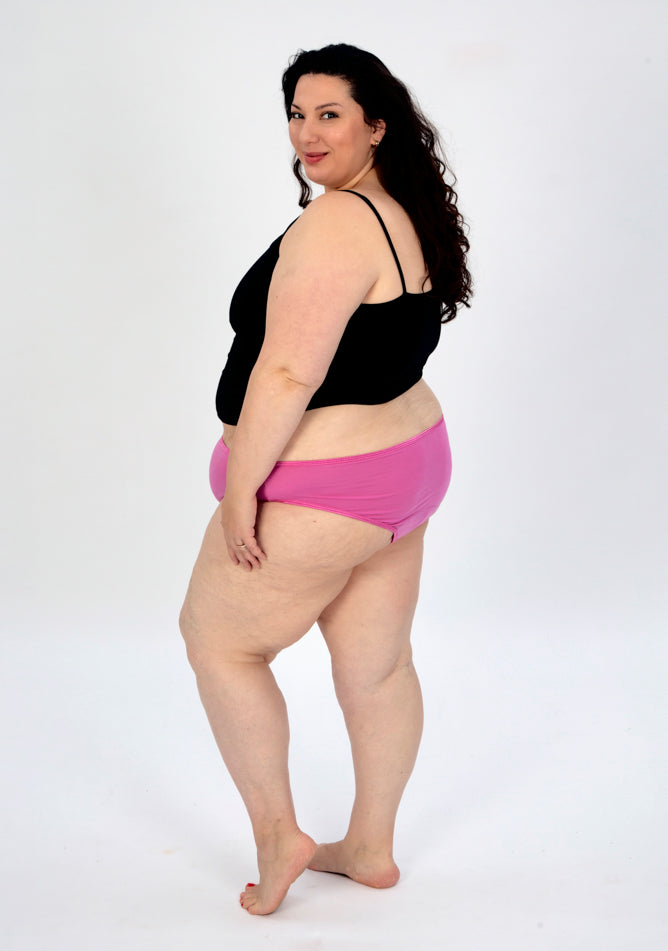 Back quarter image of a five foot seven, size 22 model wearing Ugly Pants' pink high waisted period pants in super heavy absorbency, paired with a black cami top.