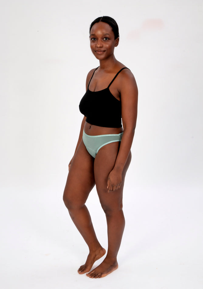 Front quarter image of a five foot four, size 10 model wearing Ugly Pants' Sage Bikini Brief period Pants in light to moderate absorbency, paired with a black crop top