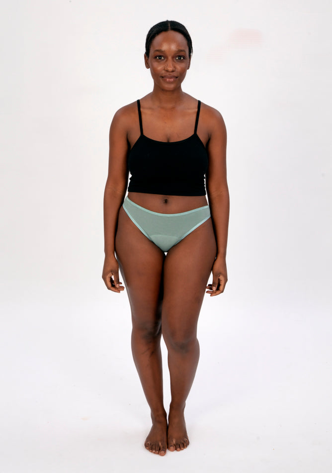 Front image of a five foot four, size 10 model wearing Ugly Pants' Sage Bikini Brief period Pants in light to moderate absorbency, paired with a black crop top