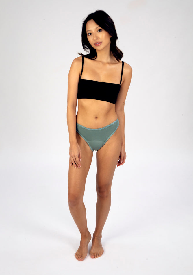 Front image of a five foot three, size 6 model wearing Ugly Pants' Sage Bikini Brief period Pants in moderate to heavy absorbency, paired with a black crop top