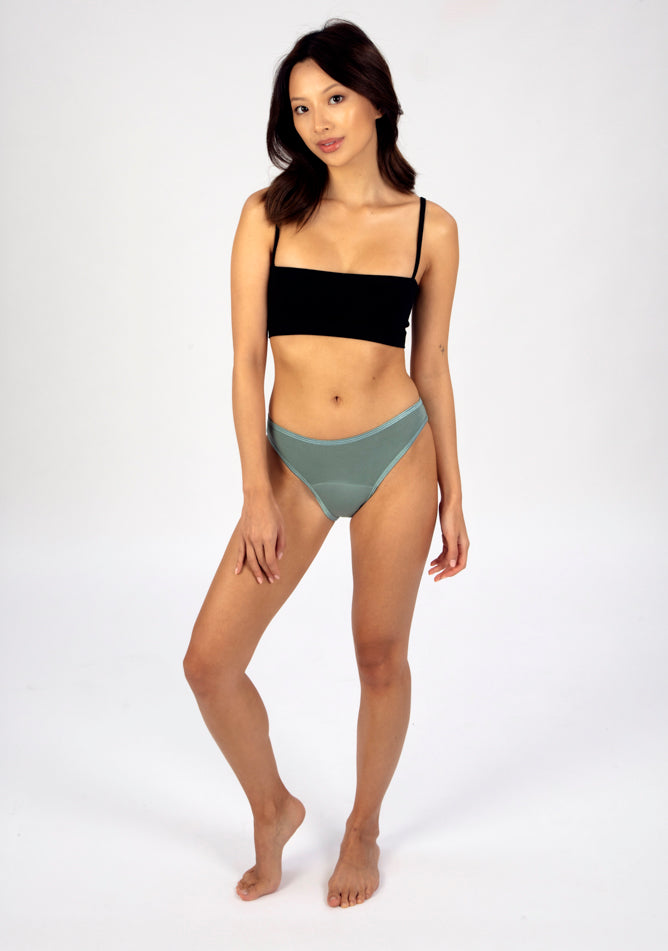 Front Quarter image of a five foot three, size 6 model wearing Ugly Pants' Sage Bikini Brief period Pants in moderate to heavy absorbency, paired with a black crop top
