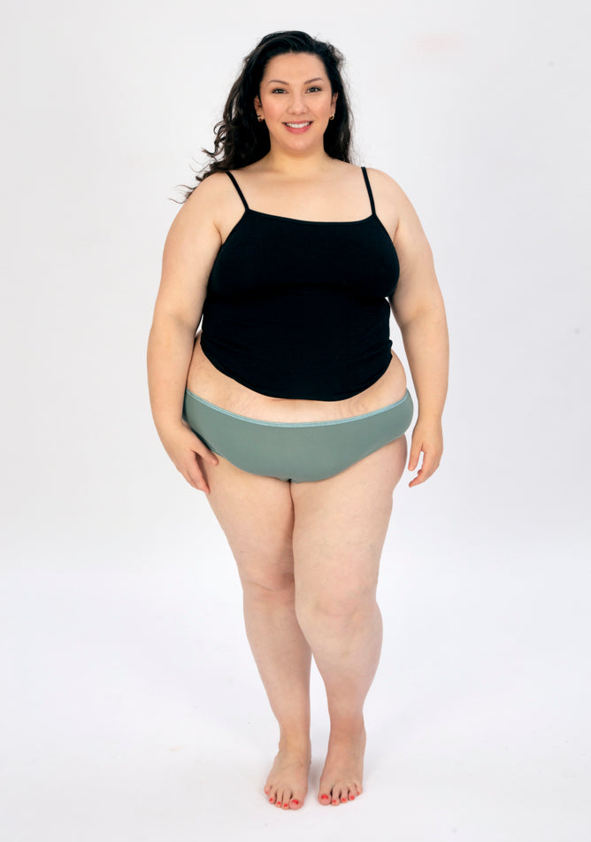 Front image of a five foot seven, size 22 model wearing Ugly Pants' sage high waisted period pants in moderate to heavy absorbency, paired with a black cami top.