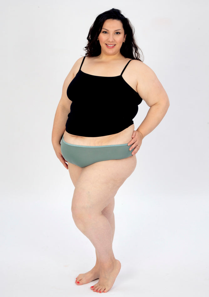 Front quarter image of a five foot seven, size 22 model wearing Ugly Pants' sage high waisted period pants in moderate to heavy absorbency, paired with a black cami top.