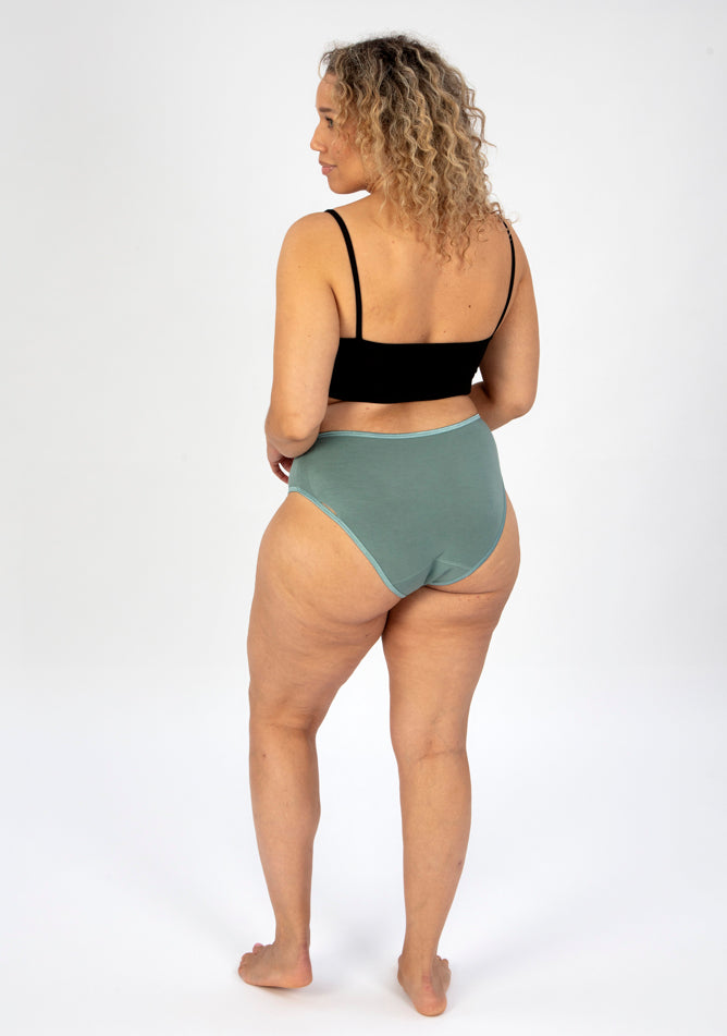 Back image of a five foot seven, size 16 model wearing Ugly Pants' sage high waisted period pants in moderate to heavy absorbency, paired with a black cami top.