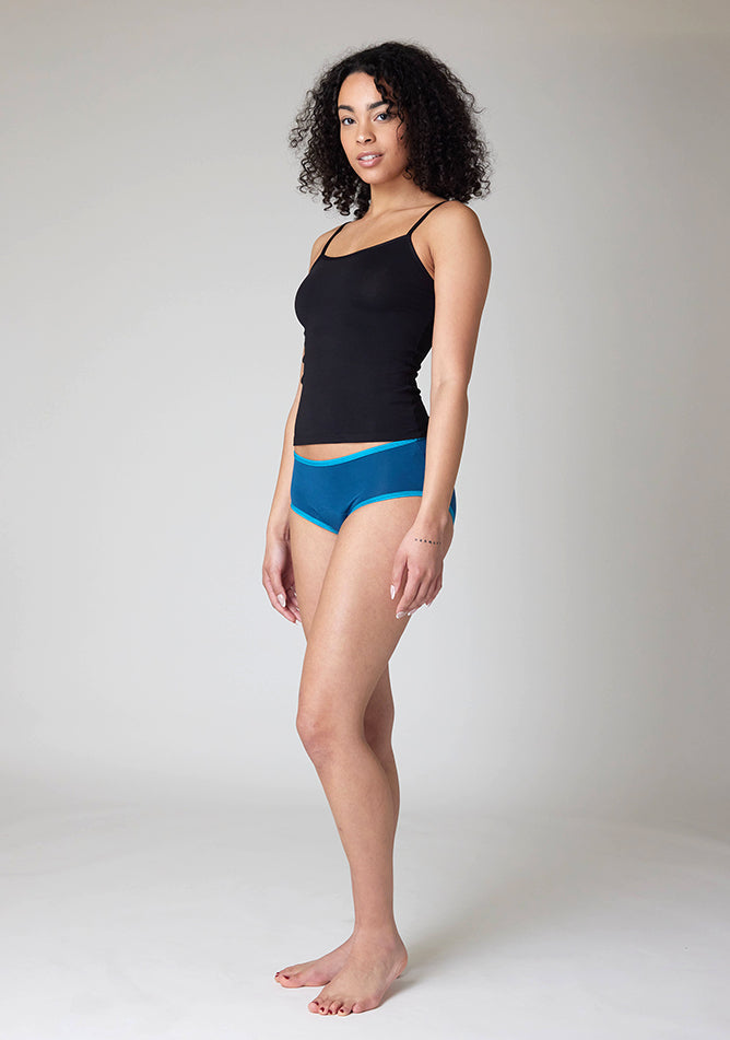 Front quarter image of a five-foot-ten, size 10 model wearing Ugly Pants' Teal Hipster Brief Period Pants in light to moderate  absorbency, paired with a black cami top