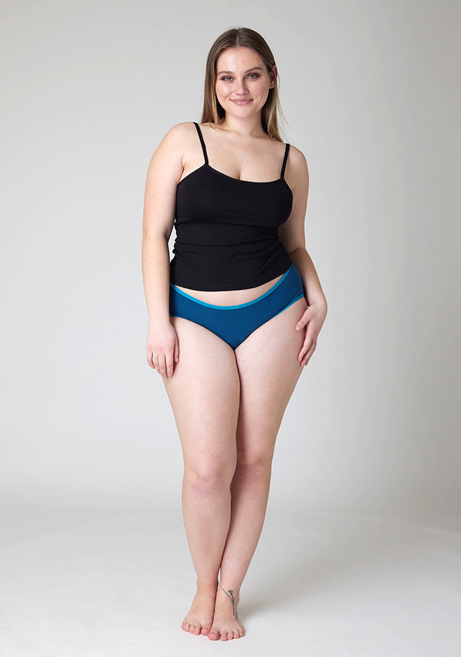 Front image of a five-foot-five, size 14 model wearing Ugly Pants' Teal Hipster Brief Period Pants in moderate to heavy absorbency, paired with a black cami top