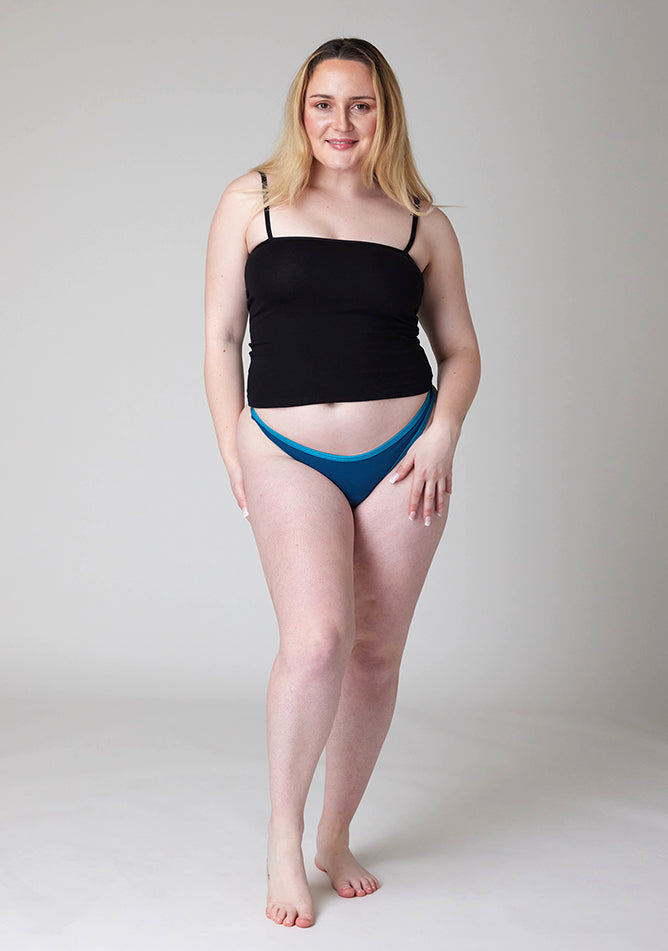 Front image of a five-foot-three, size 12 model wearing Ugly Pants' Teal Thong period pants in a light absorbency, paired with a black cami top.