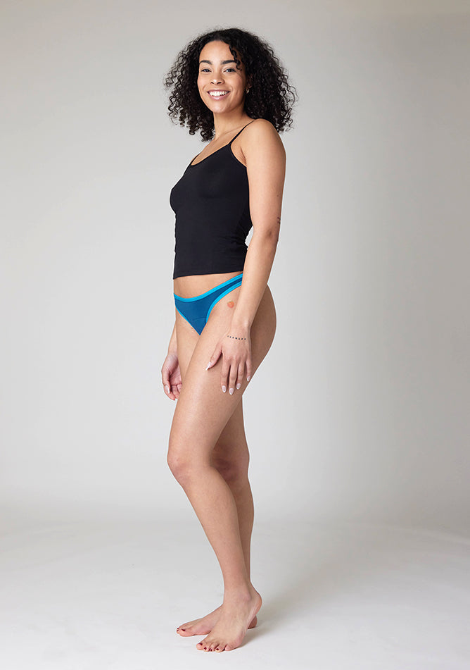 Front quarter image of a five-foot-ten, size 10 model wearing Ugly Pants' Teal Thong period pants in a light absorbency, paired with a black cami top.