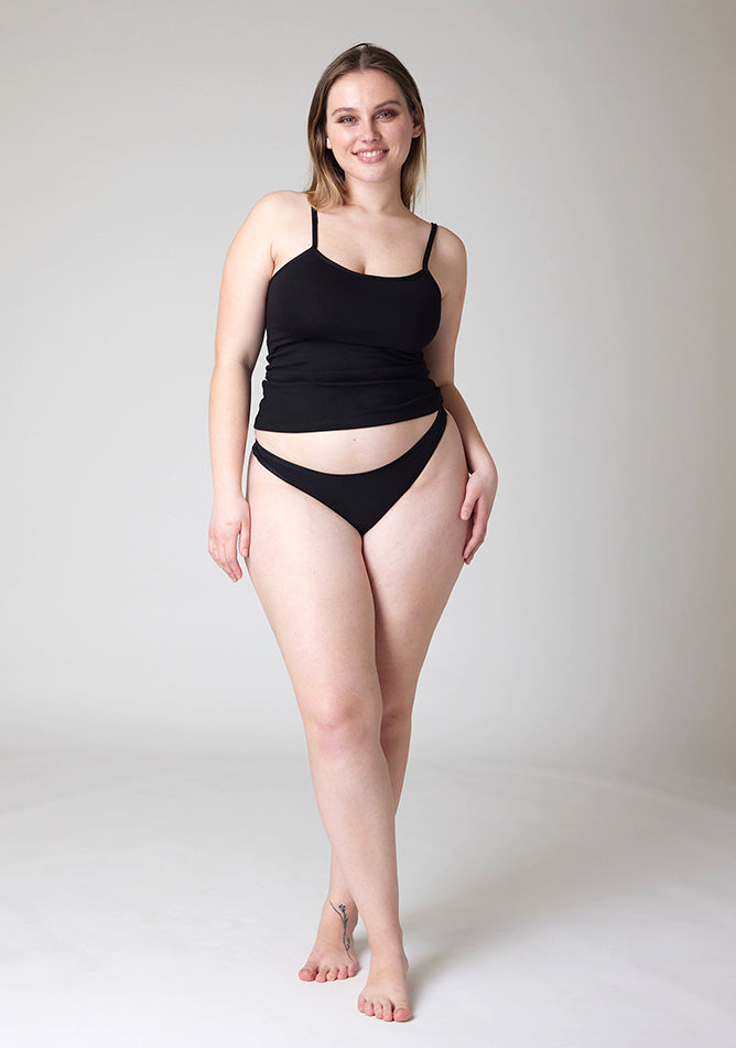 Front image of a five-foot-five, size 14 model wearing Ugly Pants' Black Thong period pants in a light absorbency, paired with a black cami top.